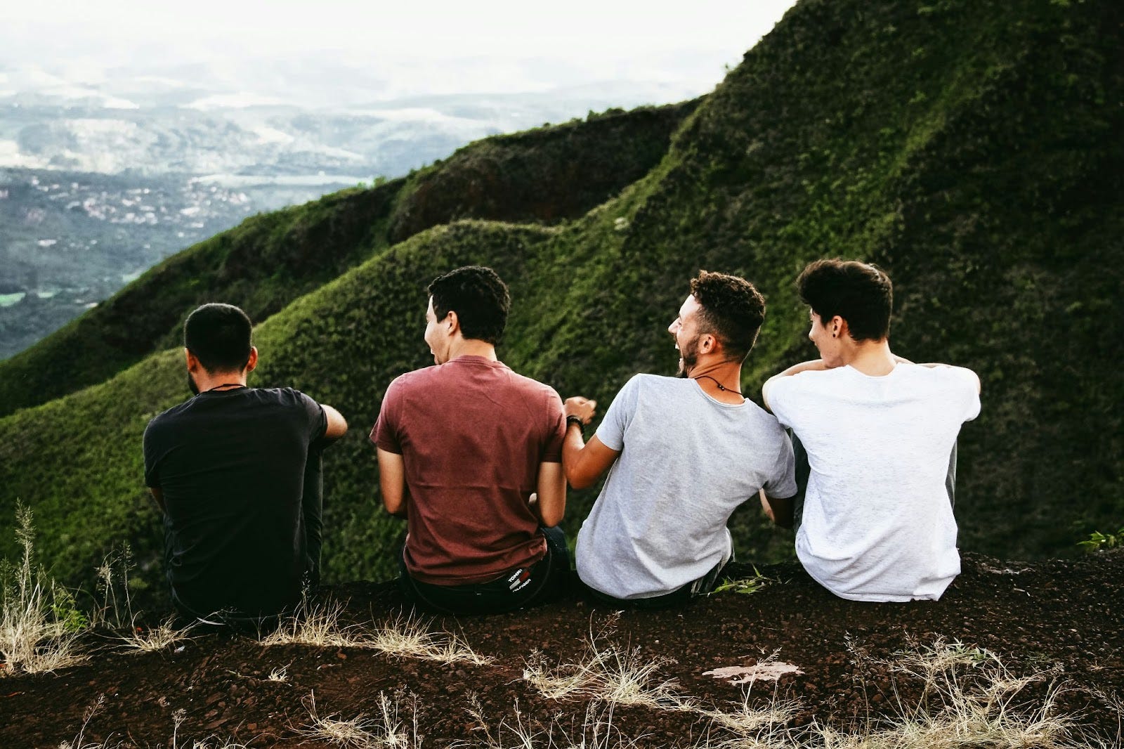 Four men sitting on the side of a hill enjoying their time together laughing