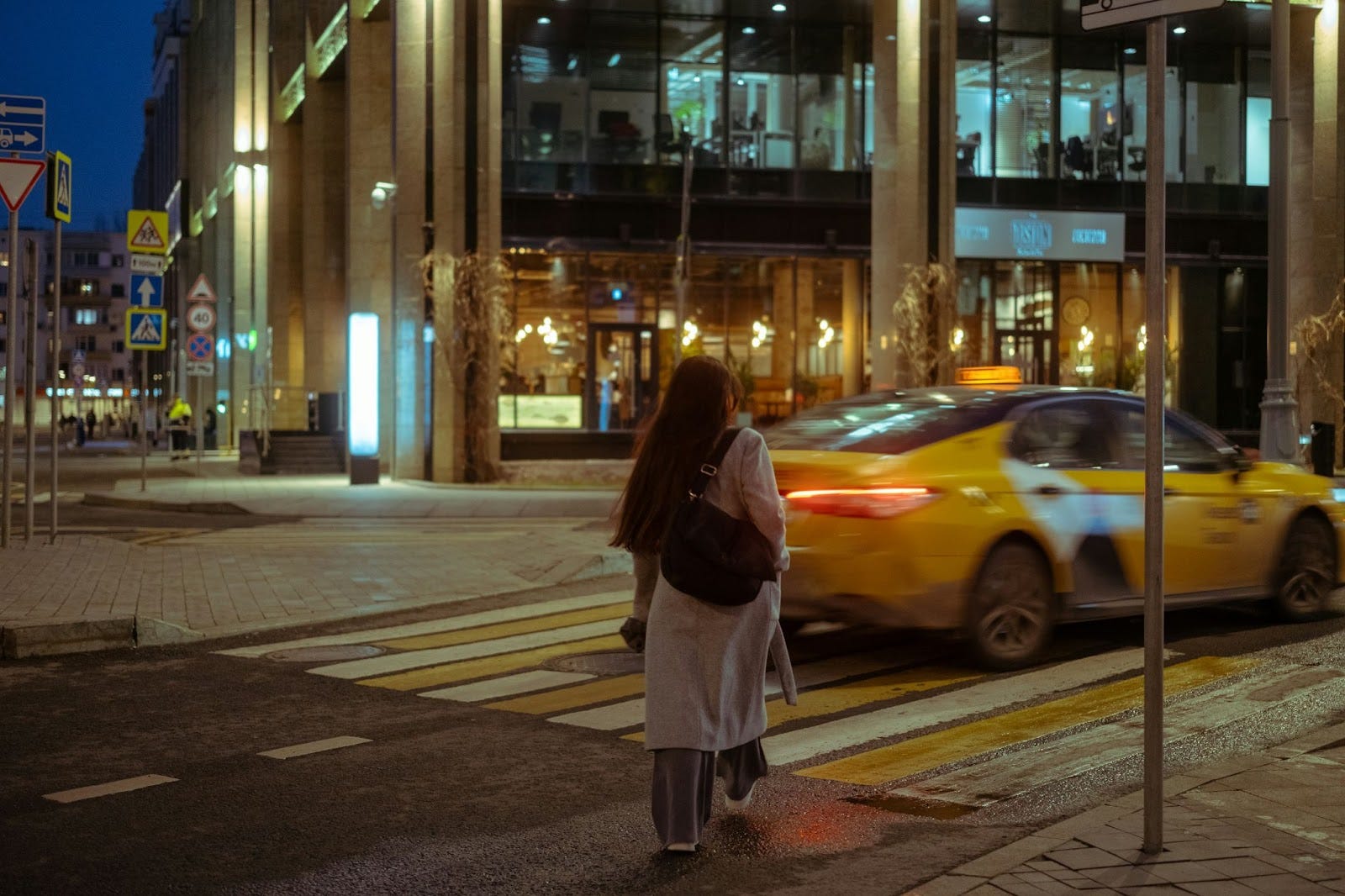 Woman walking along a city street at night as a cab drives by